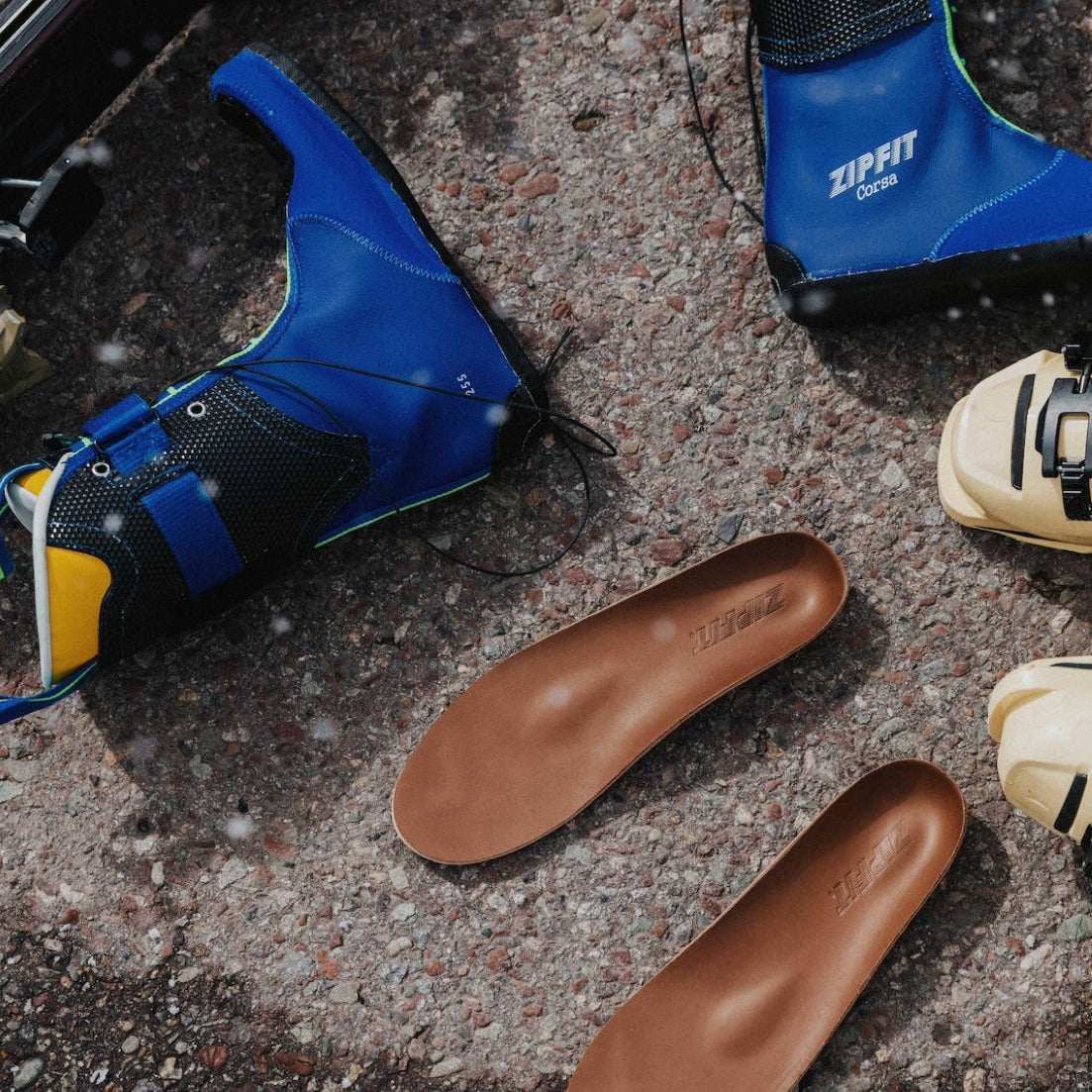Brown shoe insoles on a concrete surface with blue and yellow shoes in the background.
